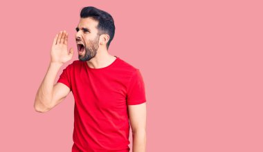 Sakallı, sıradan tişörtlü genç ve yakışıklı bir adam el pençe divan durup bağırıyor. iletişim konsepti. 