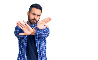 Gündelik kıyafetler giyen genç İspanyol adam. Reddedilmiş yüz ifadesi. Kollar ve avuçlar çapraz. 