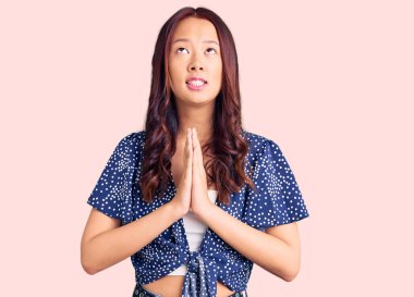 Genç, güzel Çinli bir kız, günlük kıyafetler giyip, elleri bağlı yalvarıyor ve dua ediyor. Yüzünde umut ifadesi var. Çok duygusal ve endişeli. Yalvarıyor. 