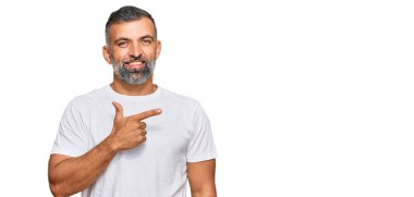 Orta yaşlı, beyaz tişört giyen, neşeli, yüzünde bir gülümseme olan yakışıklı bir adam, mutlu ve doğal bir ifadeyle elini ve parmağını yana kaldırıyor. 