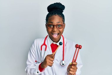 Genç Afro-Amerikan kadın doktor üniforması giymiş elinde çatal tutarak çılgınlığı kutluyor ve başarıya hayret ediyor gözleri açık heyecanla haykırıyor. 