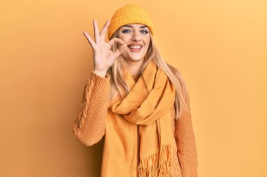 Beyaz kadın yün kazak ve şapkalı gülümsüyor. El ve parmaklarıyla tamam işareti yapıyor. başarılı ifade. 
