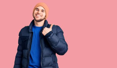 Kış kıyafetleri giyen yakışıklı adam mutlu ve pozitif gülümsüyor, başparmağıyla mükemmel ve onay işareti yapıyor. 