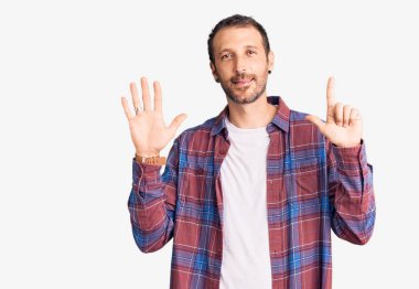 Genç ve yakışıklı bir adam gündelik giysiler giyer ve yedinci parmaklarını göstererek gülümserken kendinden emin ve mutlu olur.. 