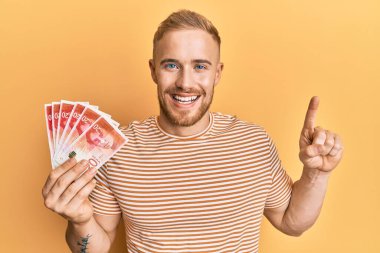 Kafkasyalı genç adam elinde 20 İsrail şekeri banknotları tutarken bir fikir veya soruyla gülümsüyor ve mutlu bir yüzle işaret ediyor. 