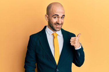 Genç İspanyol takım elbiseli ve kravatlı gülen yüzlü bir adam başparmağıyla yan tarafı işaret ediyor.. 