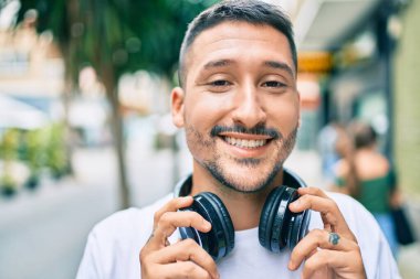 Genç İspanyol adam gülümsüyor. Mutlu bir şekilde müzik dinliyor. Şehir caddesinde kulaklık kullanıyor..