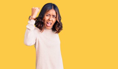 Genç, güzel, melez, balıkçı yaka kazak giyen kızgın, kızgın, yumruğunu kaldıran öfkeli ve öfkeyle bağıran kadın. öfke ve agresif konsept. 