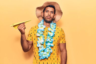 Yaz şapkası takan genç bir latin ve elinde kağıt uçak tutan Hawaii zambağı olan düşünceli ve ayık bir yüz ifadesi olan kendine güvenen bir adam. 