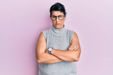 Artı, sıradan kıyafetler giyen, gözlüklü, kuşkucu ve gergin, yüzünde çapraz kollu tasvip etmeyen esmer kadın. negatif kişi. 