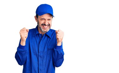 Orta yaşlı yakışıklı tamirci üniforması giyen başarılı olduğu için heyecanlı kolları havada ve gözleri kapalı zaferi kutlarken gülümsüyor. Kazanan konsept. 