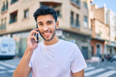 Genç Latin adam gülümsüyor ve şehirde akıllı telefondan konuşuyor..