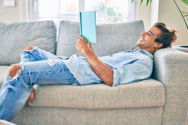 Genç İspanyol gülümseyen mutlu bir kitap okuyucu evdeki kanepede uzanıyor.