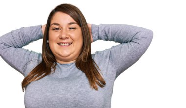 Güzel esmer, iri yarı, rahat kıyafetler giyen, esneyen, kolları ve elleri başının arkasında olan, mutlu gülümseyen bir kadın. 