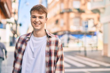 Genç beyaz adam gülümseyerek şehirde mutlu mesut duruyor..