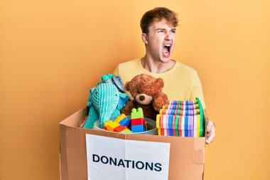 Kafkasyalı genç adam elinde oyuncaklarla dolu bir bağış kutusu tutuyor kızgın ve öfkeli çığlıklar atıyor, öfkeyle bağırıyor. öfke ve agresif konsept. 