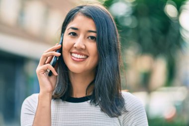 Genç İspanyol kadın gülümsüyor. Şehirdeki akıllı telefondan konuşuyor..