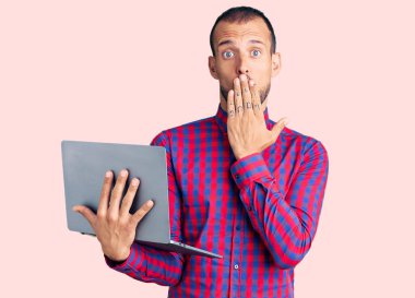 Genç yakışıklı adam bilgisayarla çalışıyor. Ağzı elle kapatıyor. Şok geçiriyor ve hata yapmaktan korkuyor. şaşırmış ifade 