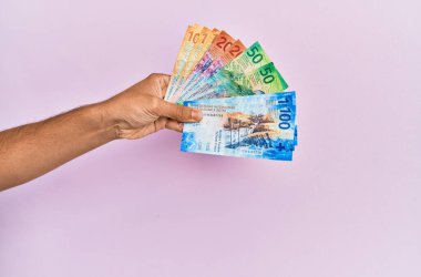 İspanyol eli İsviçre frangı banknotlarını soyutlanmış pembe arka planda tutuyor.
