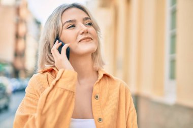 Genç sarışın kız gülümsüyor. Şehirdeki akıllı telefondan konuşuyor..