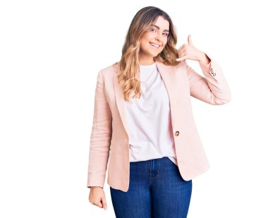 İş kıyafetleri giymiş, gülümseyen, el ve parmaklarıyla telefon hareketi yapan, telefonda konuşur gibi genç beyaz bir kadın. iletişim kavramları. 