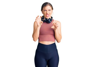 Güzel beyaz kadın spor kıyafetleri giyiyor ve kulaklık takıyor. Gülümsüyor. Kedi gibi pençe hareketi yapıyor. 