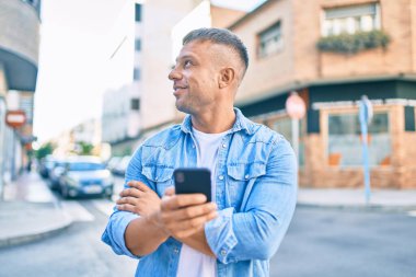 Beyaz adam şehirde akıllı telefon kullanarak mutlu bir şekilde gülümsüyor..