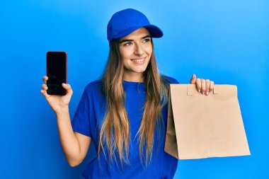 Genç İspanyol kadın, elinde kağıt torbayla akıllı telefon ekranını gösteriyor. Gülümsüyor ve kafasını çeviriyor.. 