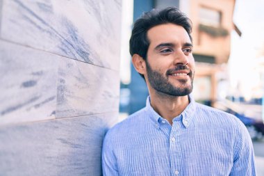 Genç İspanyol adam gülümsüyor. Mutlu bir şekilde şehrin duvarına yaslanıyor..