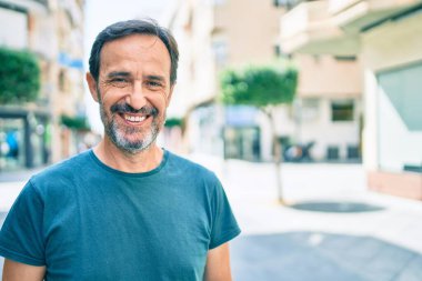 Orta yaşlı, sakallı, açık havada mutlu gülümseyen bir adam.