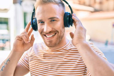 Genç İrlandalı gülümseyen mutlu müzik dinleyen şehir caddesinde kulaklık kullanan.