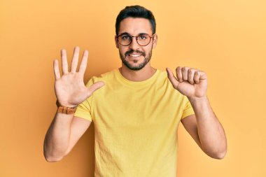 Gündelik kıyafetler giyen ve gözlük takan İspanyol genç adam altı numarayı gösterip işaret ederken kendinden emin ve mutlu gülümsüyor.. 