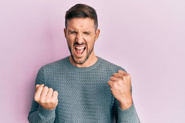 Kışlık süveter giyen yakışıklı adam kolları havada ve gözleri kapalı bir şekilde başarıyı kutluyor ve şaşırıyor. 