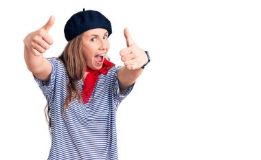 Fransız beresi takan ve çizgili tişört giyen genç, güzel sarışın kadın elinle olumlu jest yapmayı onaylıyor, gülümsüyor ve başarı için mutlu. kazanan jest. 