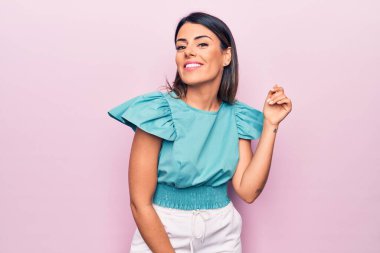 Genç ve güzel esmer kadın mutlu ve kendinden emin gülümsüyor. İzole edilmiş pembe arka planda yüzünde bir gülümsemeyle duruyorum.