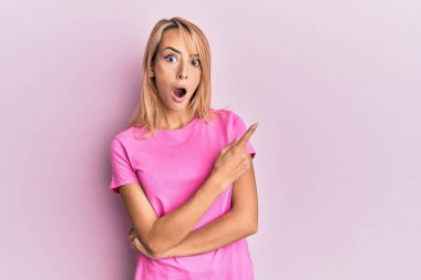 Gündelik pembe tişört giyen güzel sarışın kadın parmaklarıyla yüzünü göstererek şaşırdı, ağzı açık hayret içinde kaldı.. 