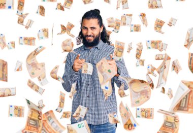 Gündelik giysiler giymiş genç bir Arap, mutlu ve komik yüzüyle kamerayı işaret ediyor. iyi enerji ve titreşimler.