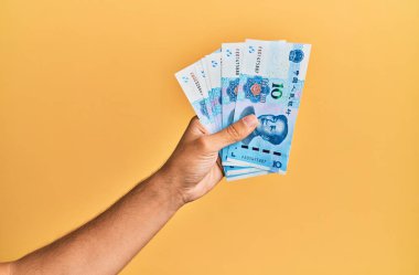 Çin malı 10 Yuan 'lık banknotları izole edilmiş sarı arka planda tutan İspanyol adamın eli..