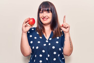 Elinde kırmızı elmayla gülümseyen genç ve cüsseli bir kadın bir fikir veya soruyla mutlu bir yüzle işaret ediyor. 