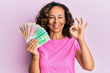 Orta yaşlı İspanyol kadın elinde Norveç kronu banknotları tutuyor. Parmaklarıyla imza atıyor, gülümsüyor. Mükemmel bir sembol. 