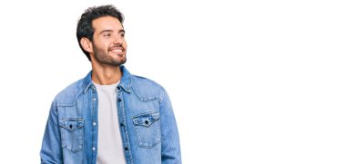 Gündelik kıyafetler giyen genç İspanyol bir adam yüzünde gülümsemeyle yan yana bakıyor, doğal bir ifade. Kendinden emin gülen. 