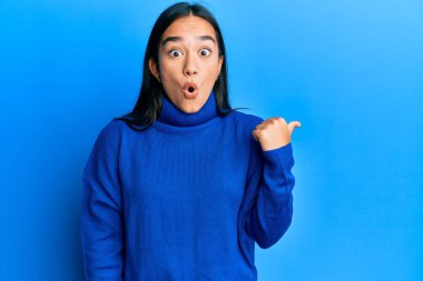 Kış süveteri giyen Asyalı genç bir kadın elini yana uzatarak şaşırdı, ağzı açık hayret içinde kaldı.. 