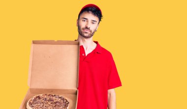 İspanyol asıllı genç bir adam elinde pizza kutusu tutarken düşünceli ve ayık bir ifade takınırken kendinden emin görünüyor. 