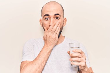 Genç yakışıklı kel adam bir bardak su içerek ağzını eliyle kapadı, şok oldu ve hata yapmaktan korktu. şaşırmış ifade 