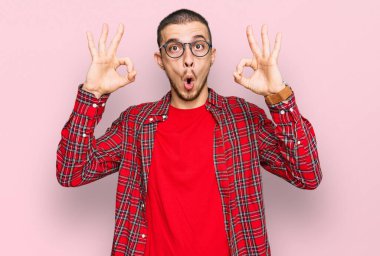 Gündelik kıyafetler giyen İspanyol genç adam şaşırmış ve şok olmuş görünüyor tamam onay sembolünü parmaklarıyla yapıyor. çılgın ifade 