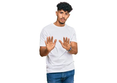 Gündelik beyaz tişört giyen genç bir Arap. Avuçlarını hareket ettiriyor. Korkmuş ve iğrenç bir ifadeyle reddediyor. Dur ve yasakla. 