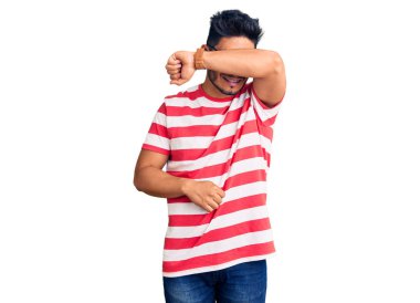 Yakışıklı Latin Amerikalı genç adam günlük kıyafetler ve gözlük takıyor. Gözleri kollarıyla kaplıyor. Neşeli ve komik gülümsüyor. kör kavram. 