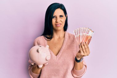 Norveç Krona banknotları elinde tutan beyaz bir kadın ve kumbaranın hiçbir fikri yok ve kafası karışık bir ifade. şüphe kavramı. 
