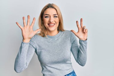 Gündelik giysiler giyen genç beyaz kadın sekiz numarayı gösterip işaret ederken kendinden emin ve mutlu bir şekilde gülümsüyor.. 
