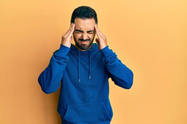 Stres yüzünden başı ağrıyan Latin kökenli genç bir adam günlük kıyafetler giyiyor. migren ağrısı. 